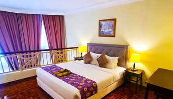 Quarto de hotel com uma cama grande, duas luminárias de cabeceira, um quadro na parede e uma varanda com cortinas.