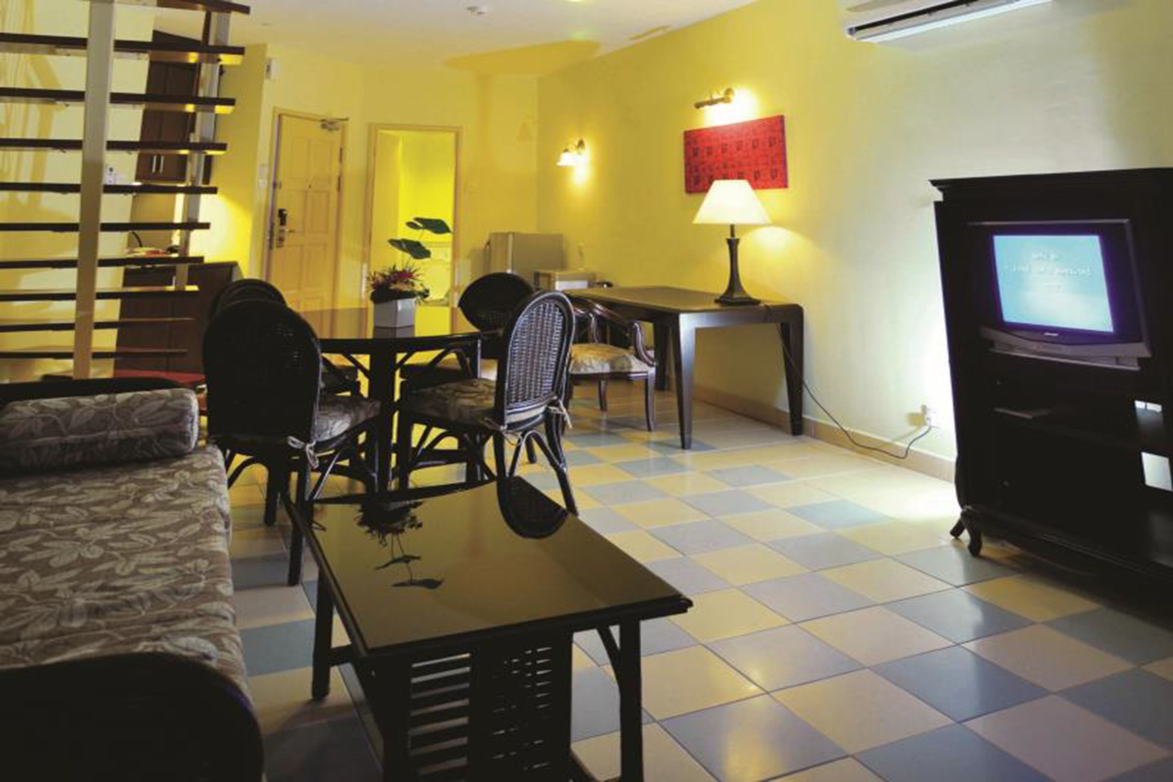 Ein Wohnzimmer mit Schachbrettboden, einer Couch, einem Esstisch mit Stühlen, einem Fernseher und einer Treppe.