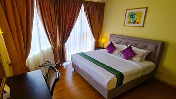A hotel room with a bed, curtains, a desk, and a lamp.