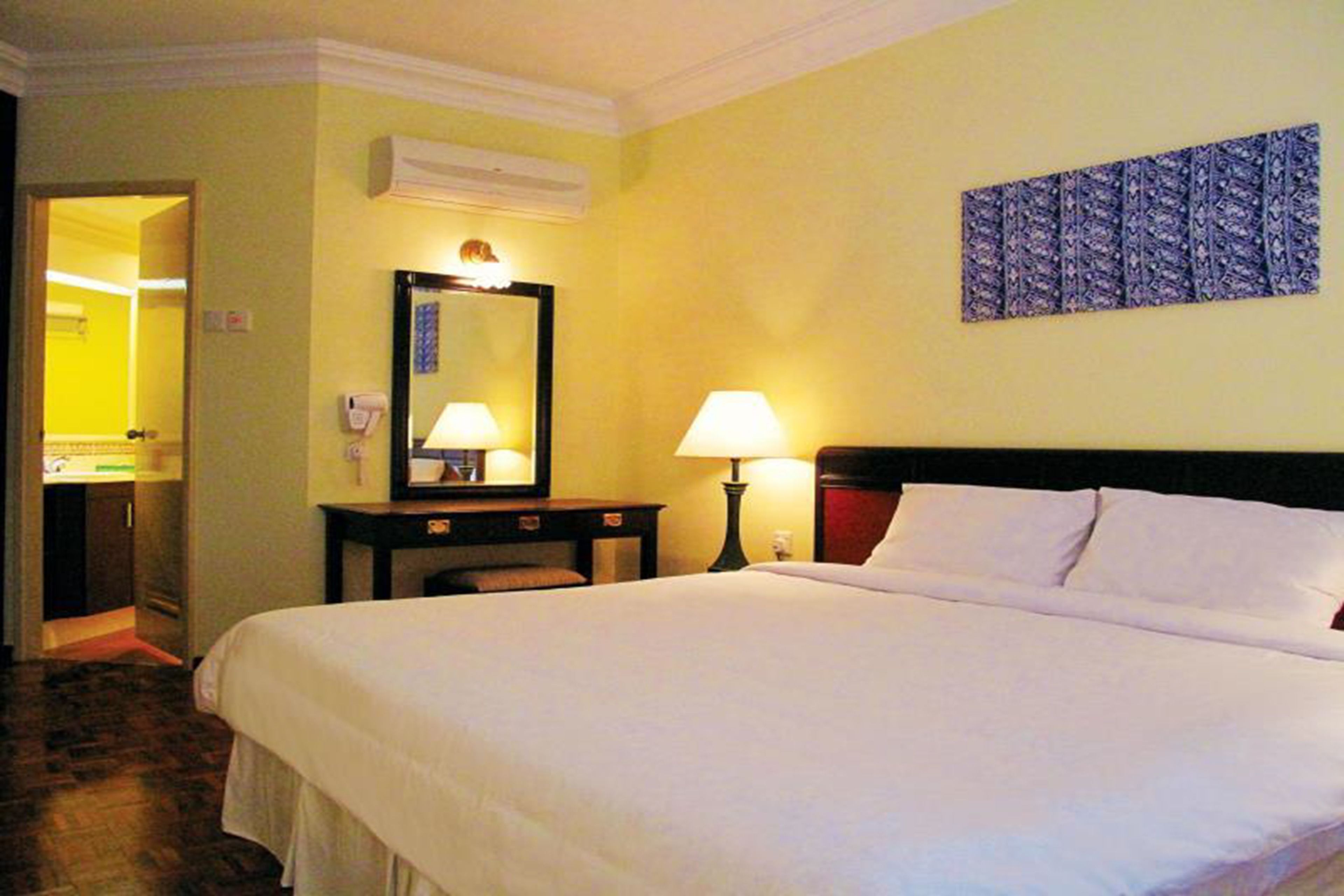 Quarto de hotel com uma cama grande, duas luminárias de cabeceira, um espelho e uma obra de arte na parede.