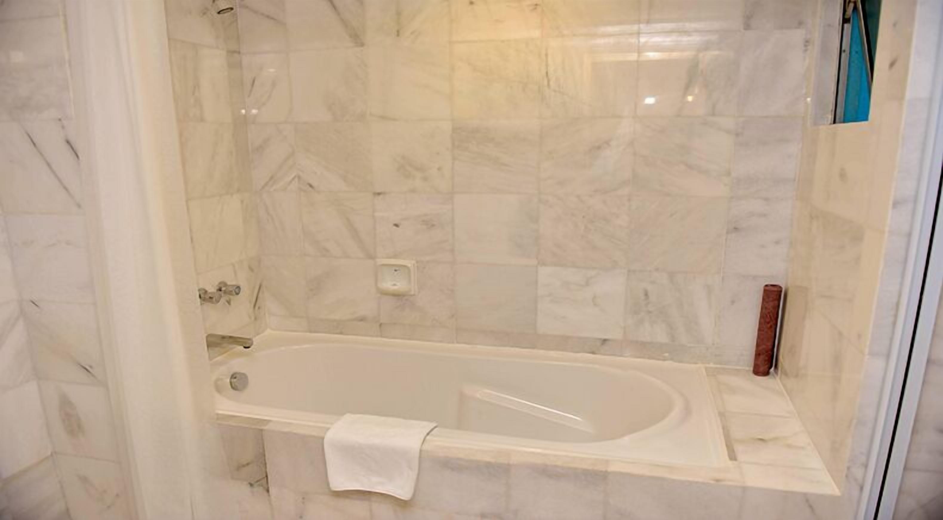 Ein Badezimmer mit Duschwand aus Marmorfliesen, einer Badewanne und einem weißen Handtuch am Rand.