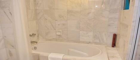 Ein Badezimmer mit Duschwand aus Marmorfliesen, einer Badewanne und einem weißen Handtuch am Rand.