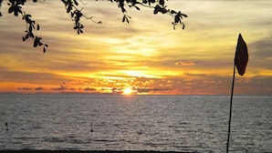 Un coucher de soleil sur l’océan, avec un drapeau flottant au sommet d’un mât.