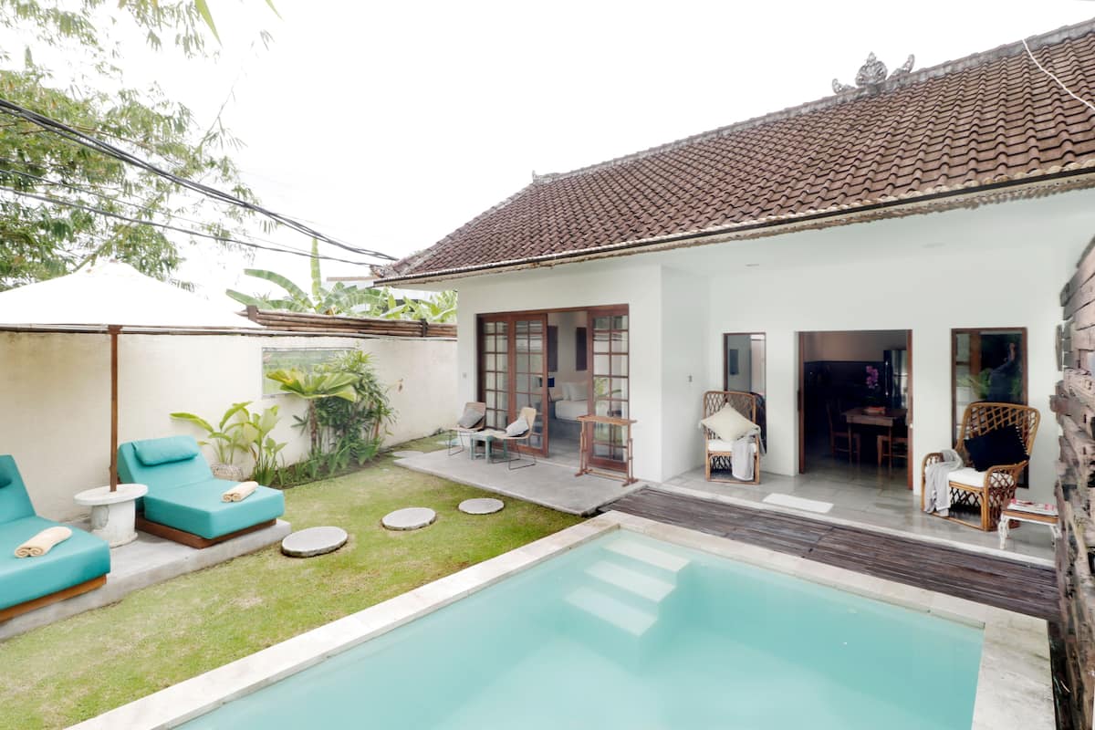 A poolside area with a swimming pool, lounge chairs, and a patio with a table and chairs.