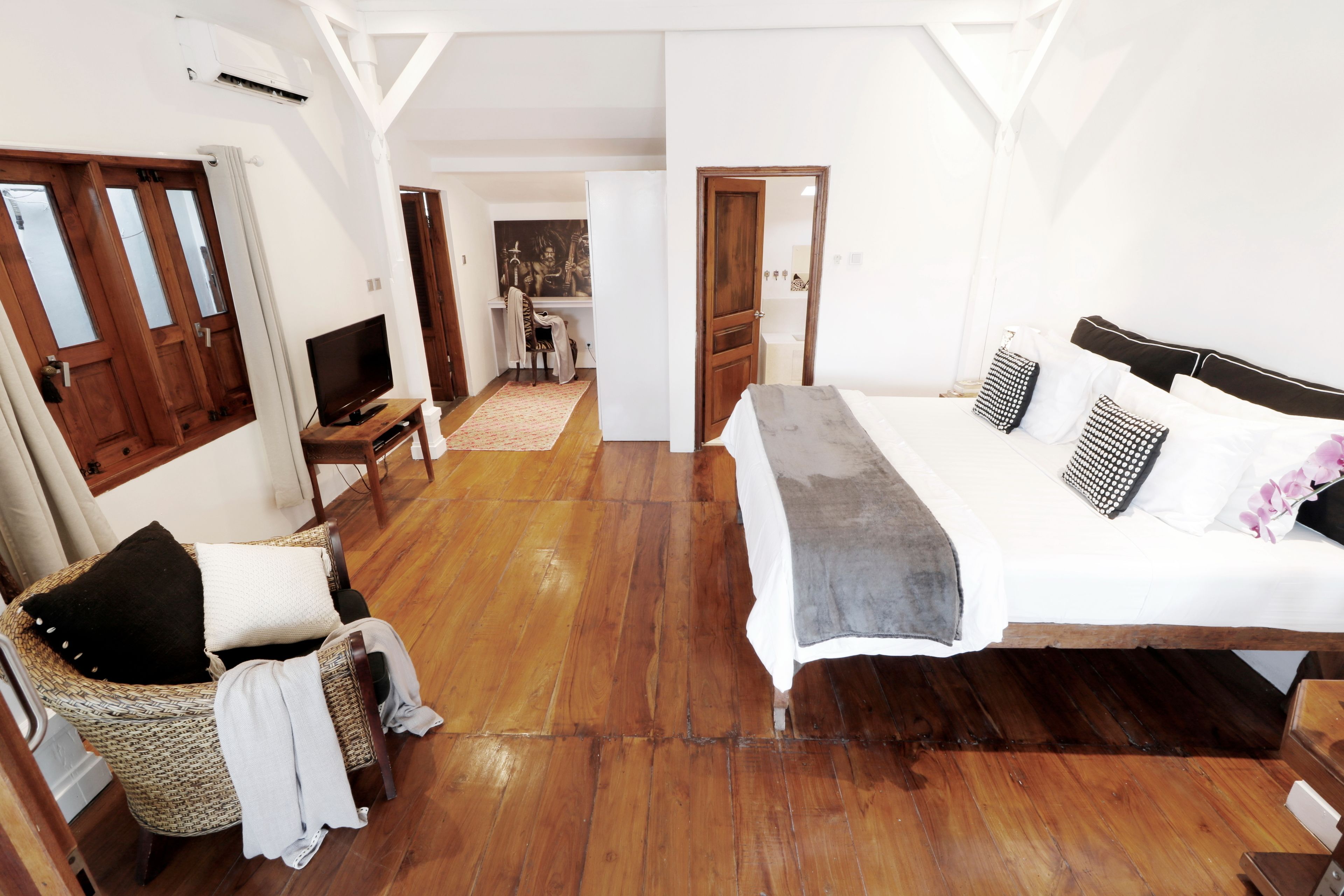 Een slaapkamer met een groot bed, een televisie, een rieten stoel en een houten vloer.