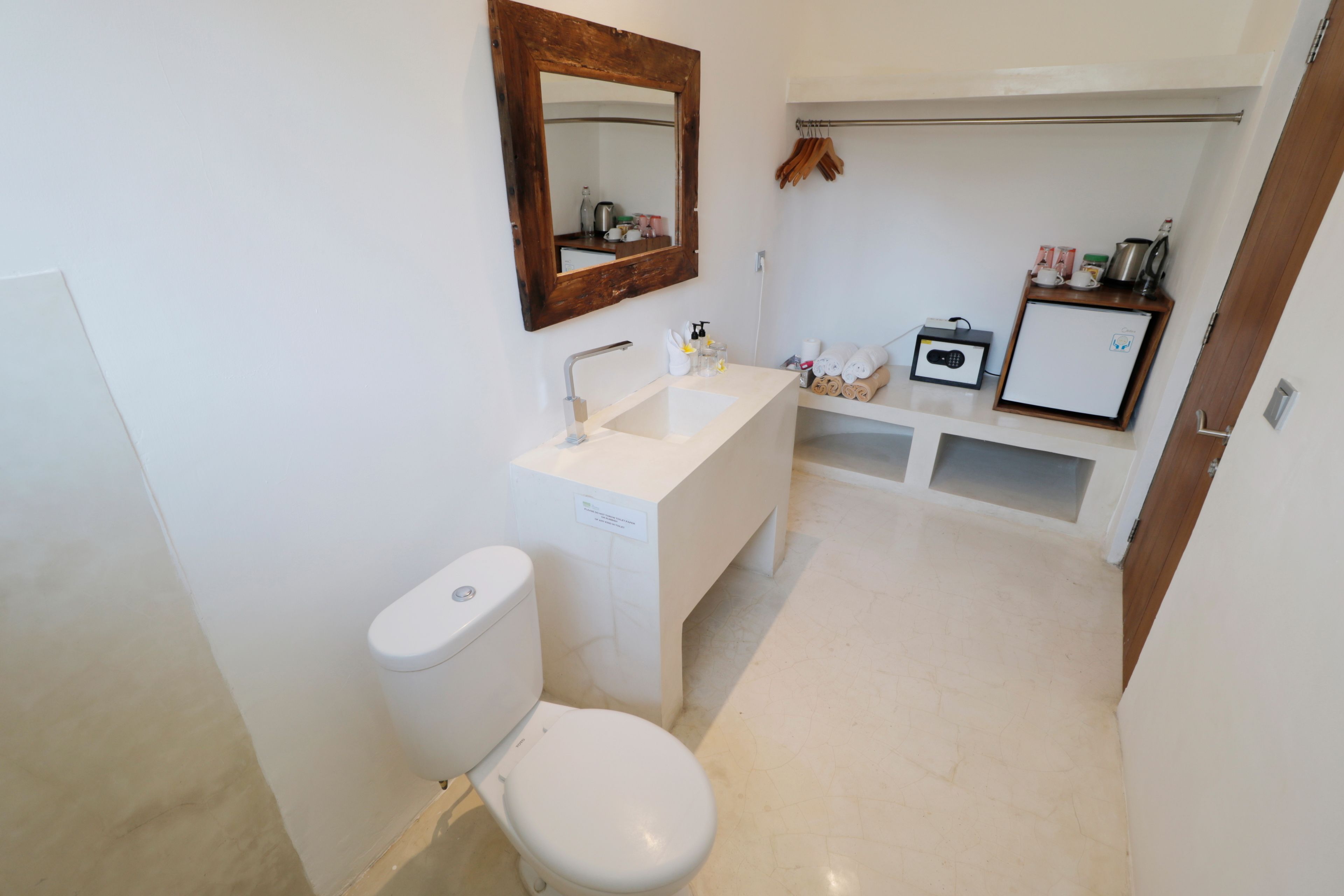 Une petite salle de bain avec des toilettes blanches, un lavabo et un miroir. On peut voir un porte-serviettes et une petite étagère avec des articles de toilette.