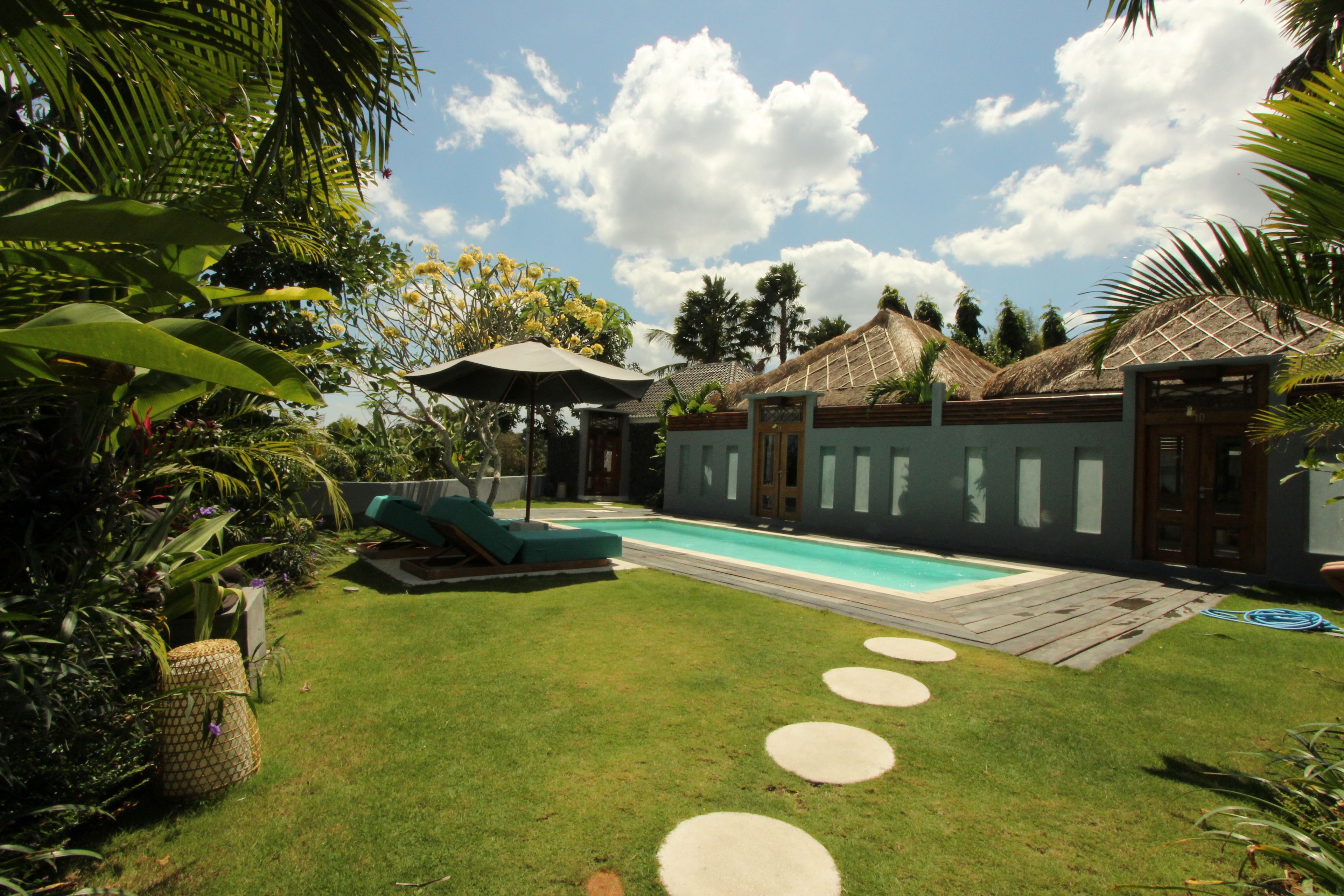 Un patio trasero con piscina, sillas de descanso y una estructura de techo de paja.
