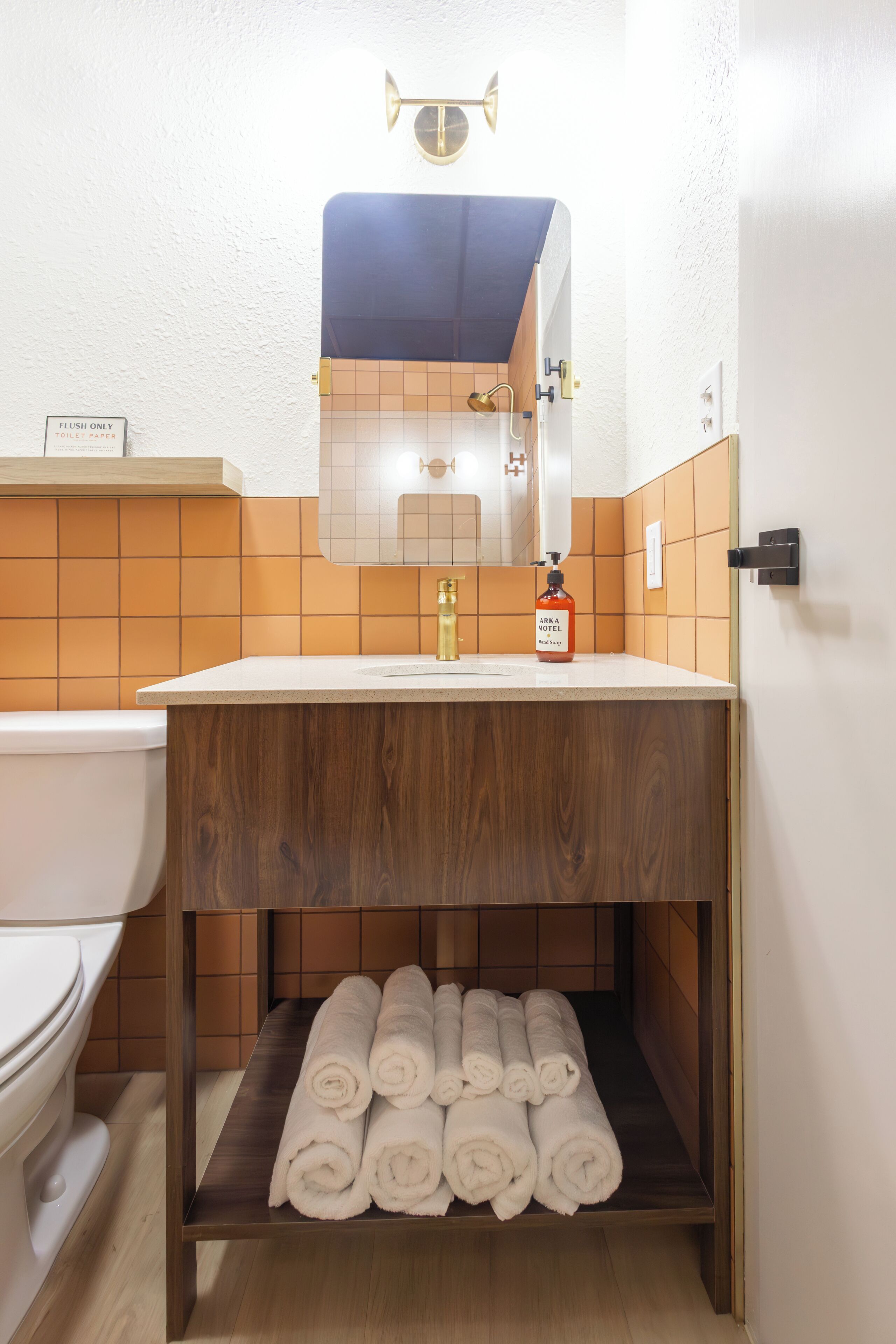 Een badkamer met toilet, wastafel, spiegel en een plank met opgerolde handdoeken.