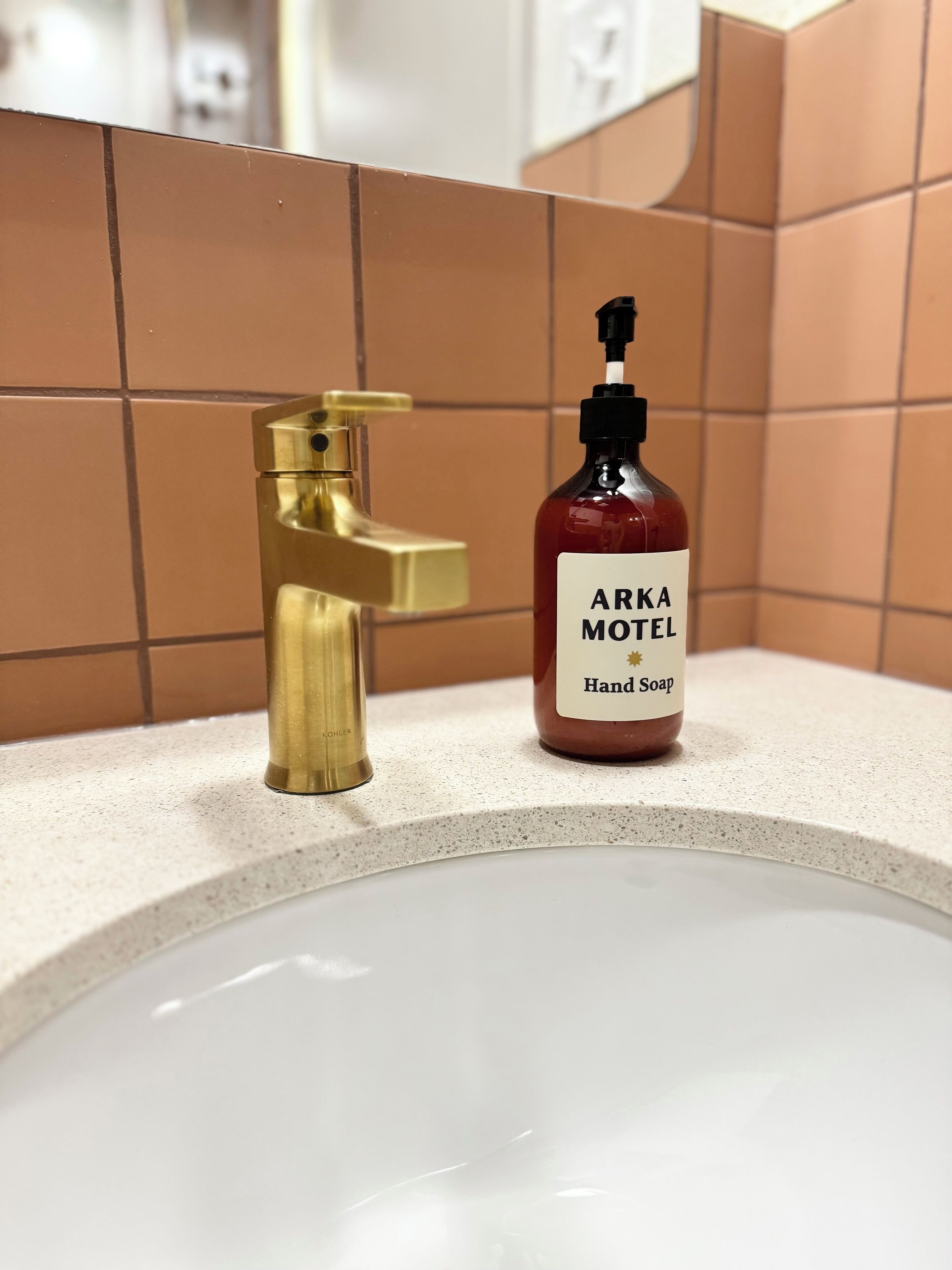 A bathroom sink with a gold faucet and a bottle of Arka Motel hand soap.
