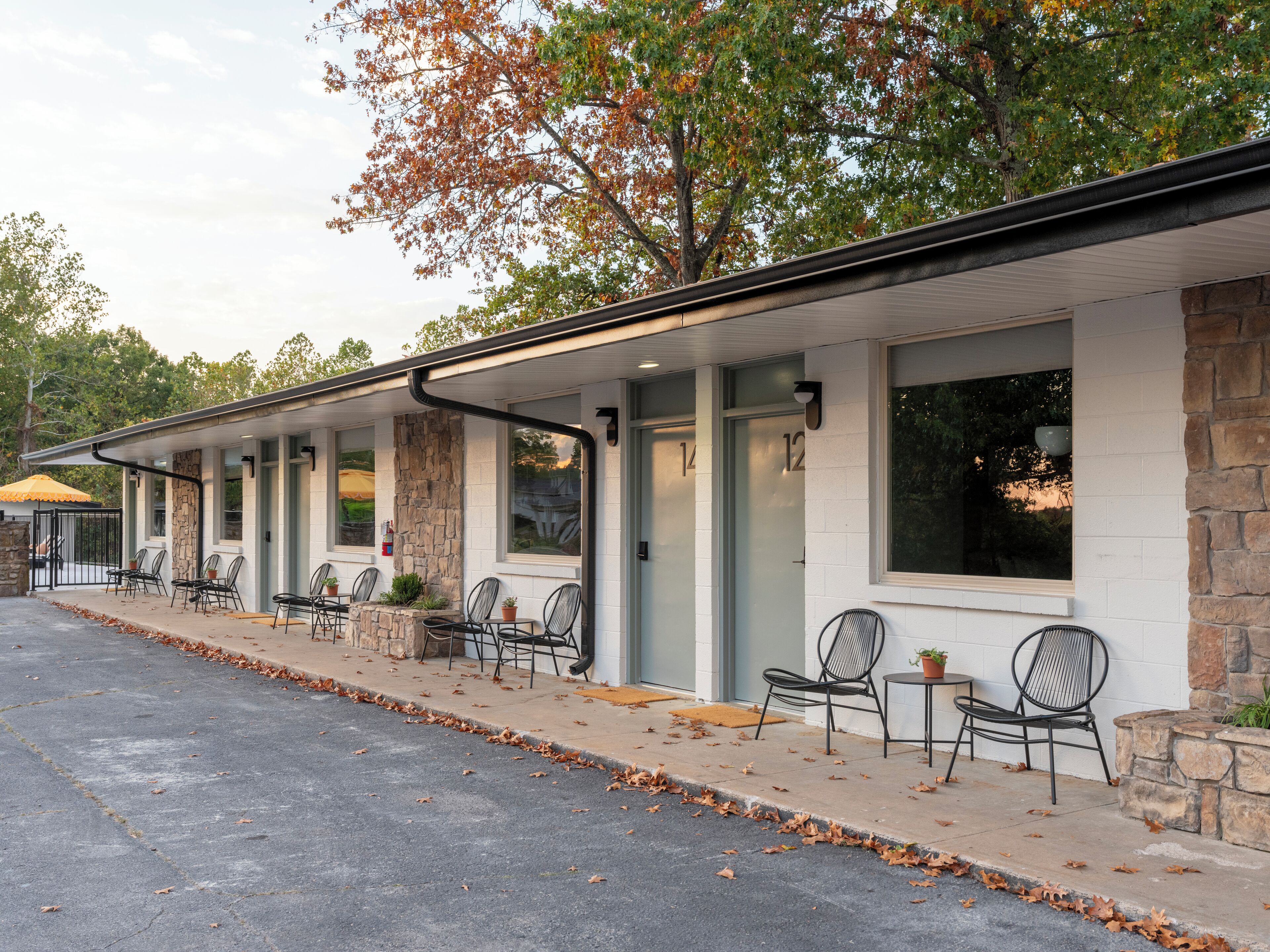 Un motel con una hilera de habitaciones, mobiliario exterior, detalles de piedra y un patio cubierto.