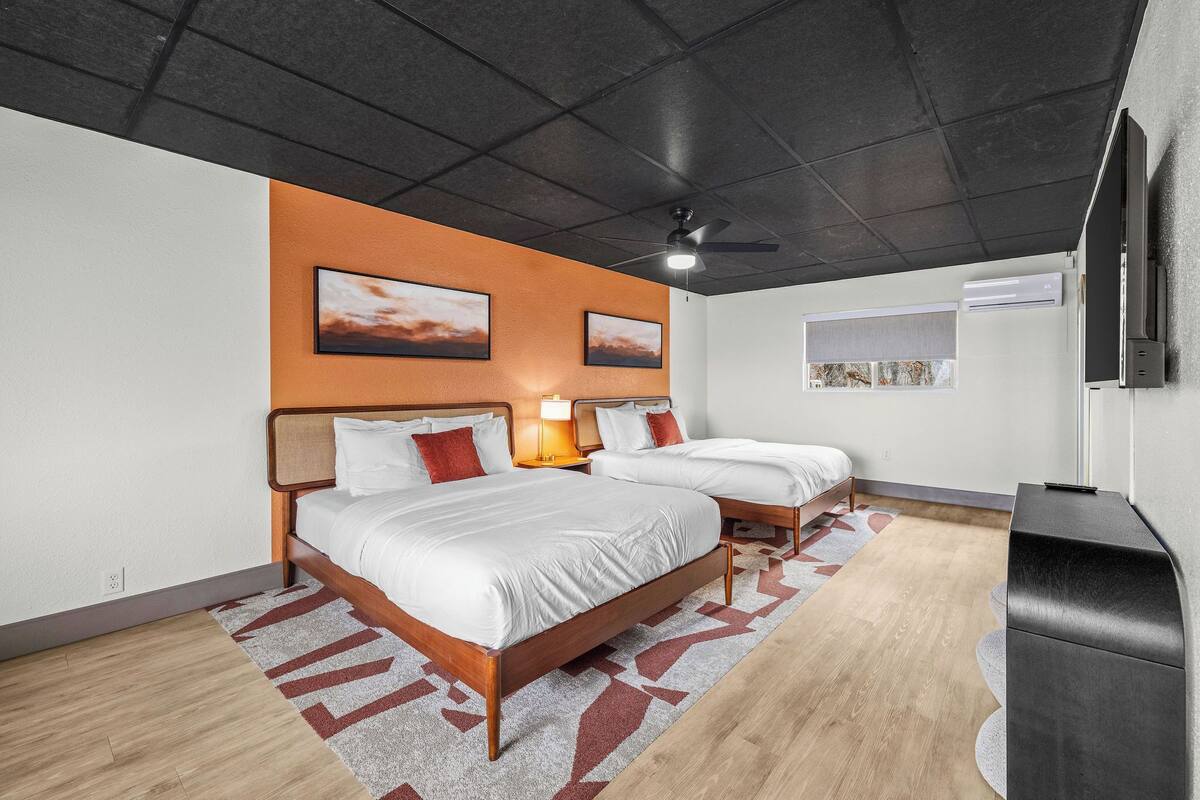 Une chambre d’hôtel avec deux lits, un ventilateur de plafond, une télévision et des œuvres d’art accrochées aux murs.