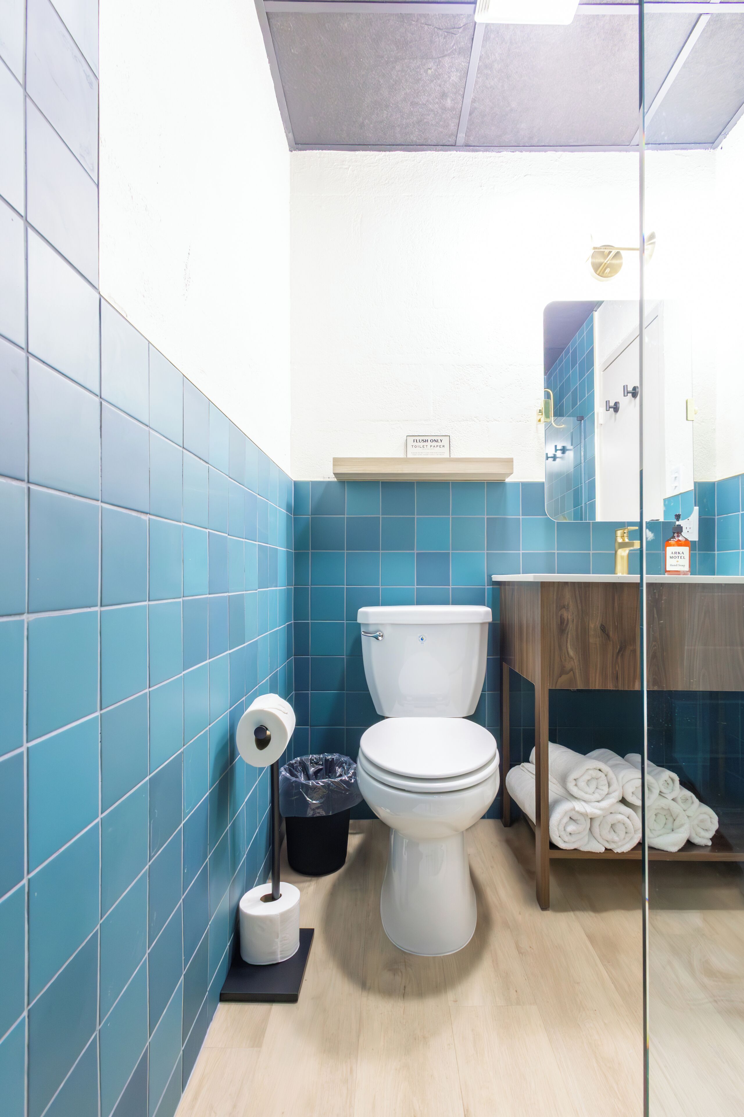 A bathroom with blue tiles, a white toilet, a wooden vanity, and a towel rack.