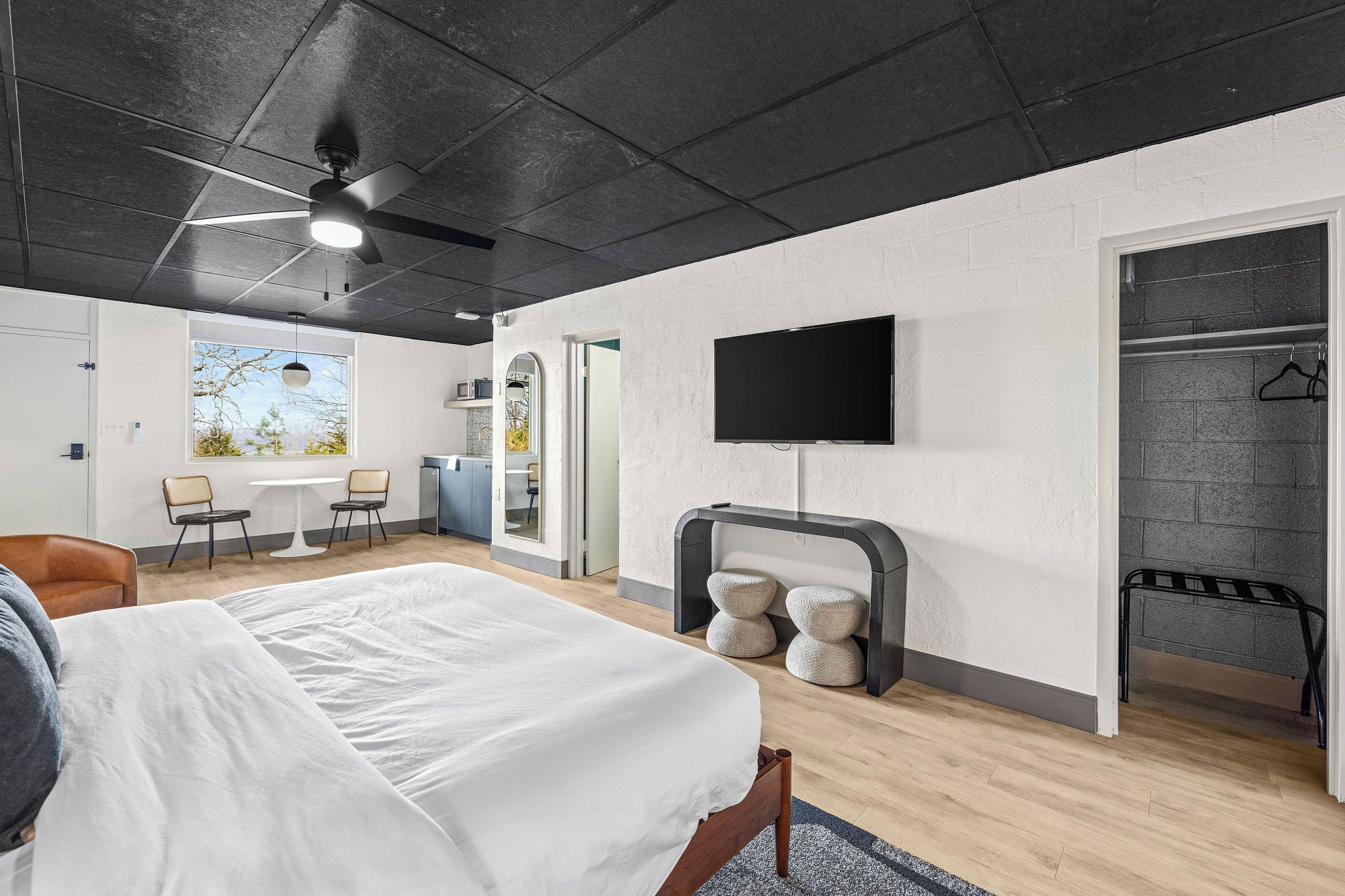 A modern hotel room with a bed, a TV, a seating area with chairs, and a view of the outdoors.
