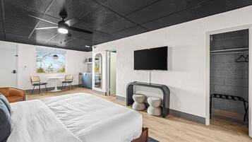 A modern hotel room with a bed, a TV, a seating area with chairs, and a view of the outdoors.