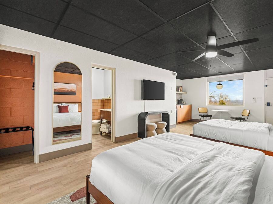 A modern hotel room with two beds, a TV, a ceiling fan, and a window with a view.