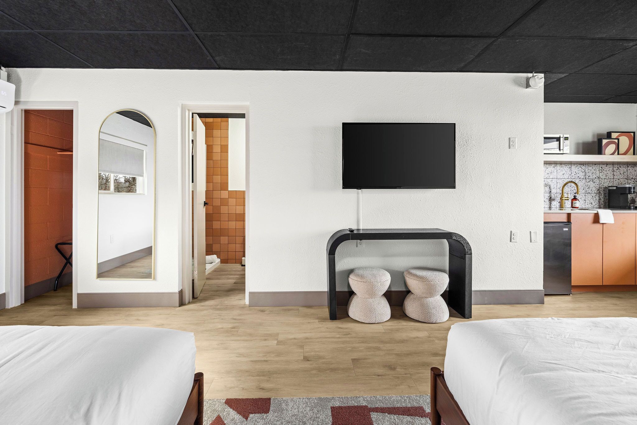 A modern hotel room with two beds, a flat-screen TV, a fireplace, and a kitchen area.