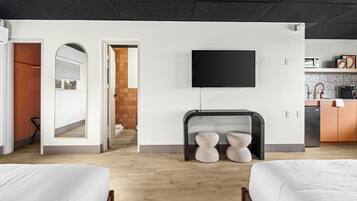 A modern hotel room with two beds, a flat-screen TV, a fireplace, and a kitchen area.