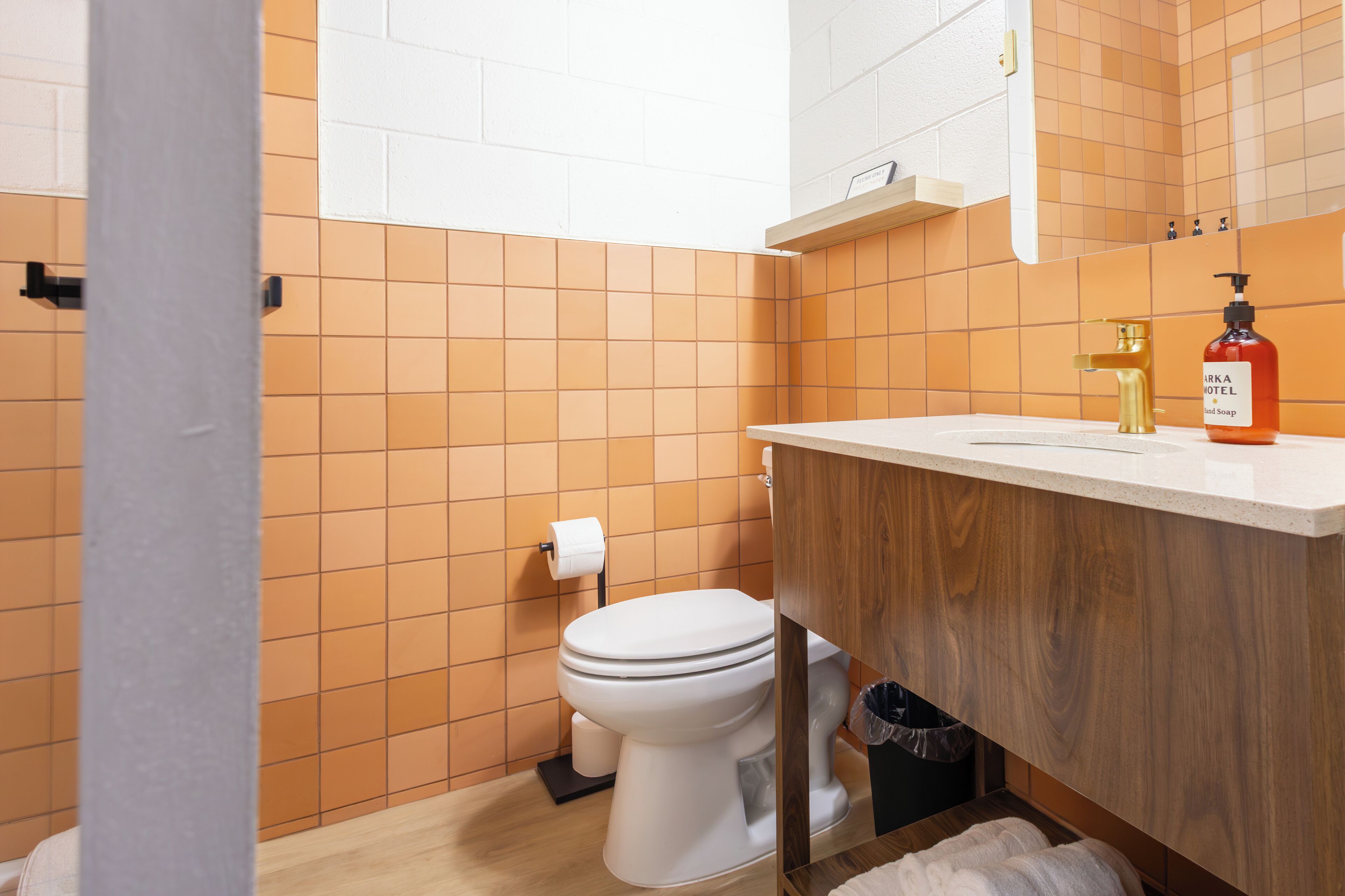 Une salle de bain avec des murs recouverts de carreaux orange, des toilettes blanches, un meuble-lavabo en bois avec un évier et un distributeur de savon pour les mains.