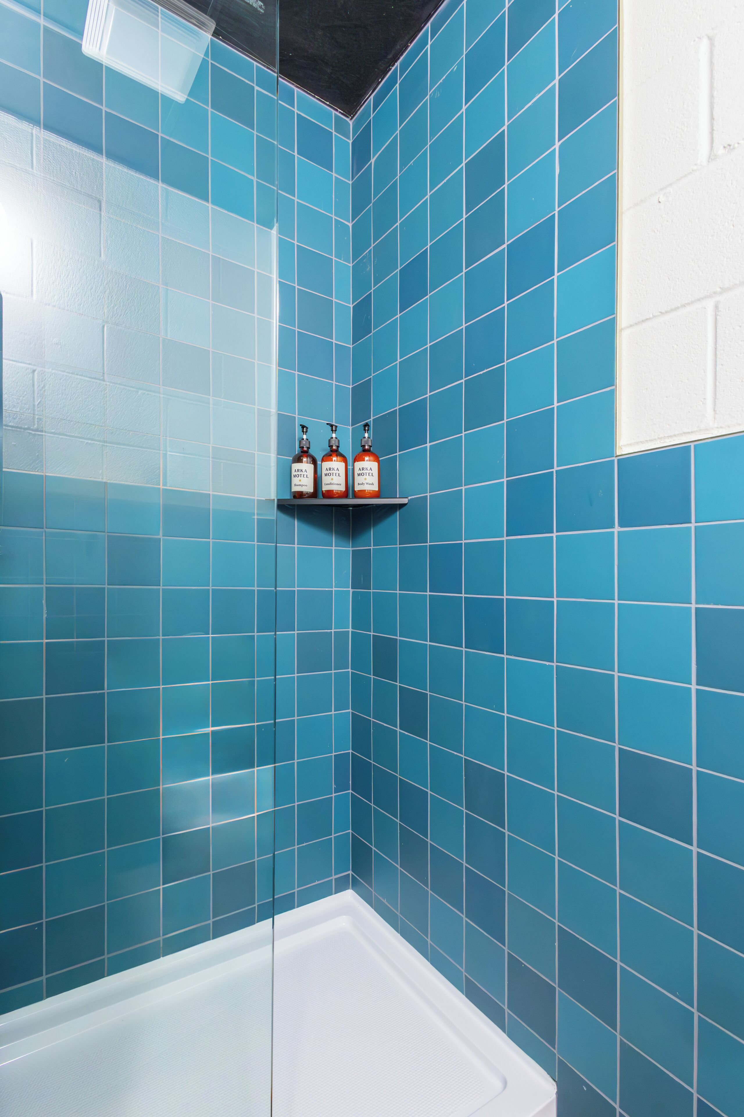 Un baño con azulejos azules, una bañera blanca y un estante con tres botellas.