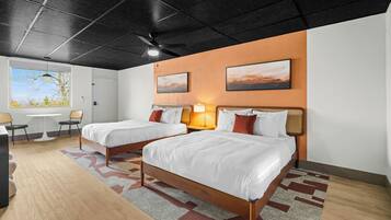 Habitación de hotel con dos camas, un escritorio, sillas, un ventanal con vistas y obras de arte en las paredes.