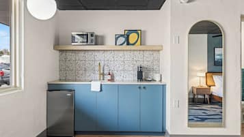 Cocina compacta con microondas, pileta y pequeño refrigerador. Hay un estante de madera sobre la encimera con un cuadro enmarcado.