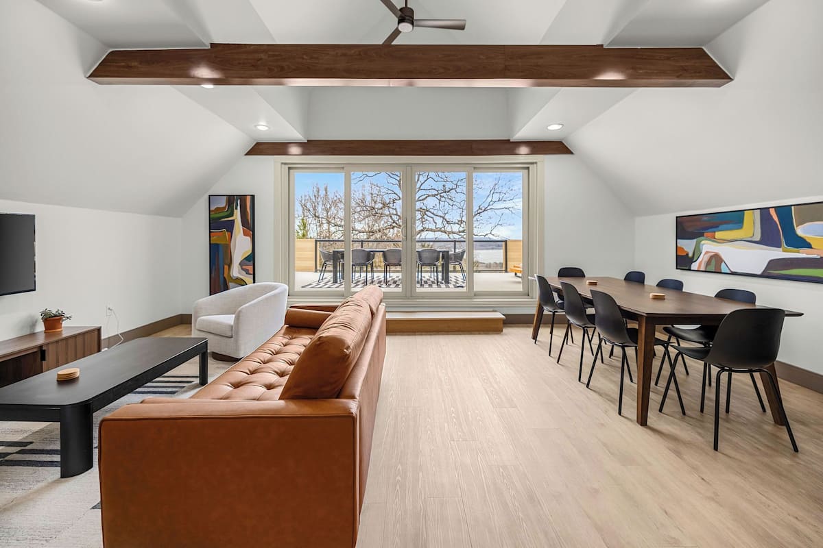Un salon moderne avec un canapé en cuir marron, une table à manger avec des chaises et une grande fenêtre donnant sur l’extérieur.