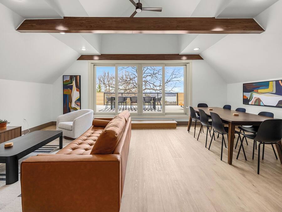 A modern living room with a brown leather sofa, a dining table with chairs, and a large window with a view of the outdoors.