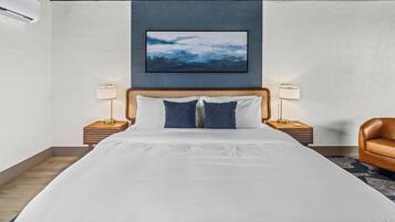 A hotel room with a large bed, two bedside tables with lamps, a brown leather chair, and a framed picture on the wall.