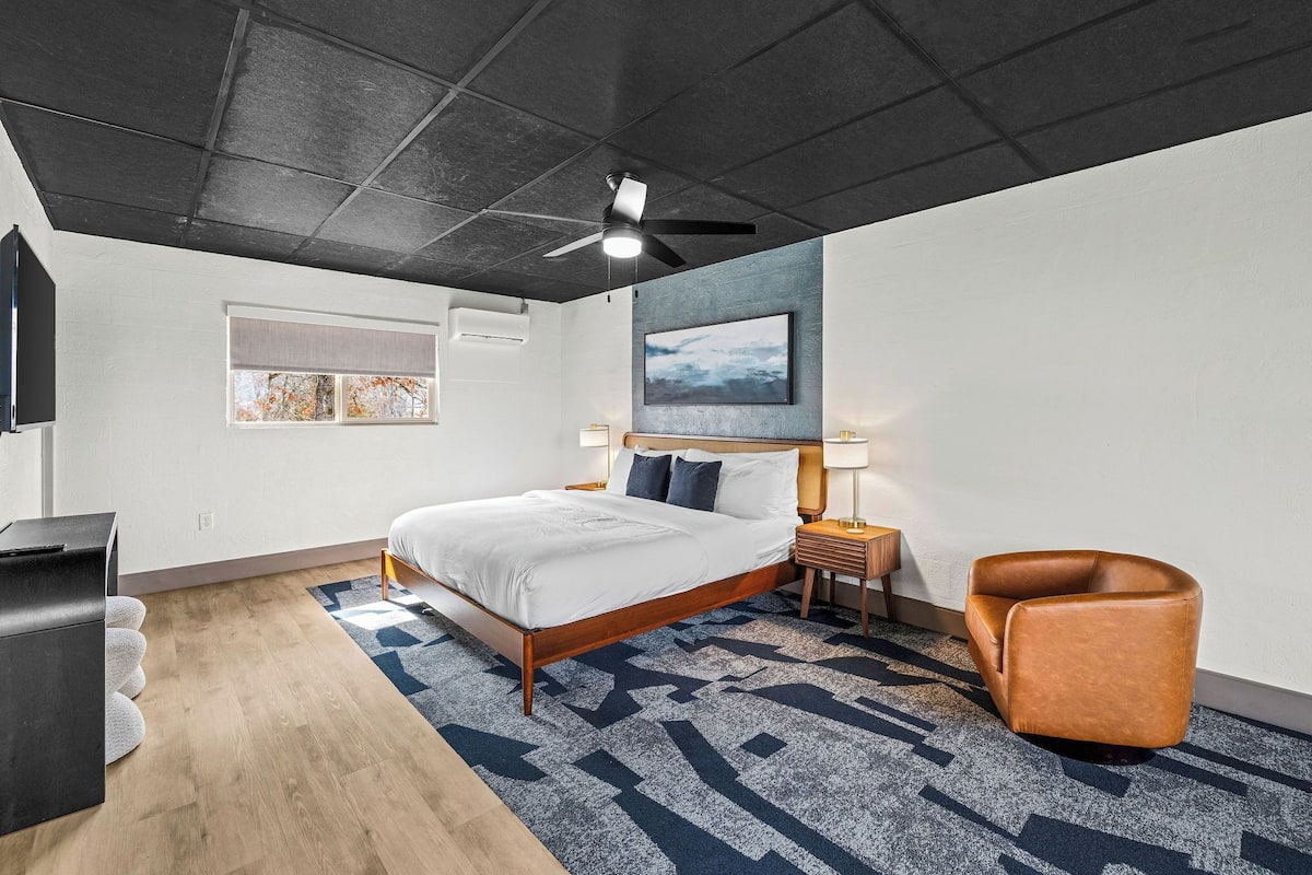 Une chambre d’hôtel moderne, équipée d’un lit, d’un bureau, d’une chaise, d’un ventilateur de plafond et d’un tableau au mur.