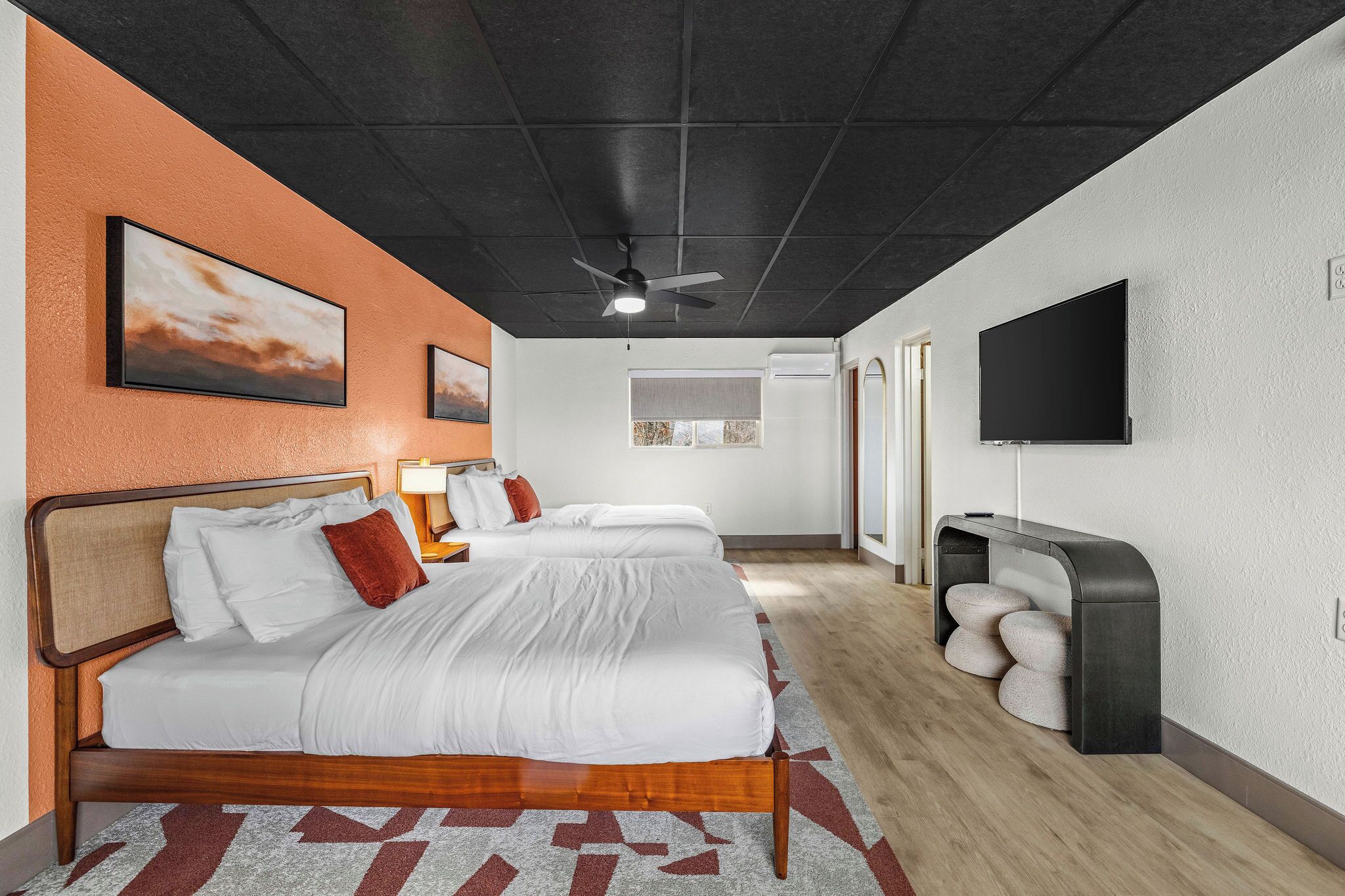 A hotel room with a bed, a ceiling fan, a TV, and a small seating area with cushions.