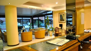 A hotel reception area with a wooden reception desk, several yellow armchairs, and potted plants. - Hotel 24 (Punta del Este)