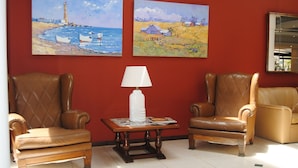 A room with two leather armchairs, a table with a lamp, and two paintings on the wall. - Hotel 24 (Punta del Este)