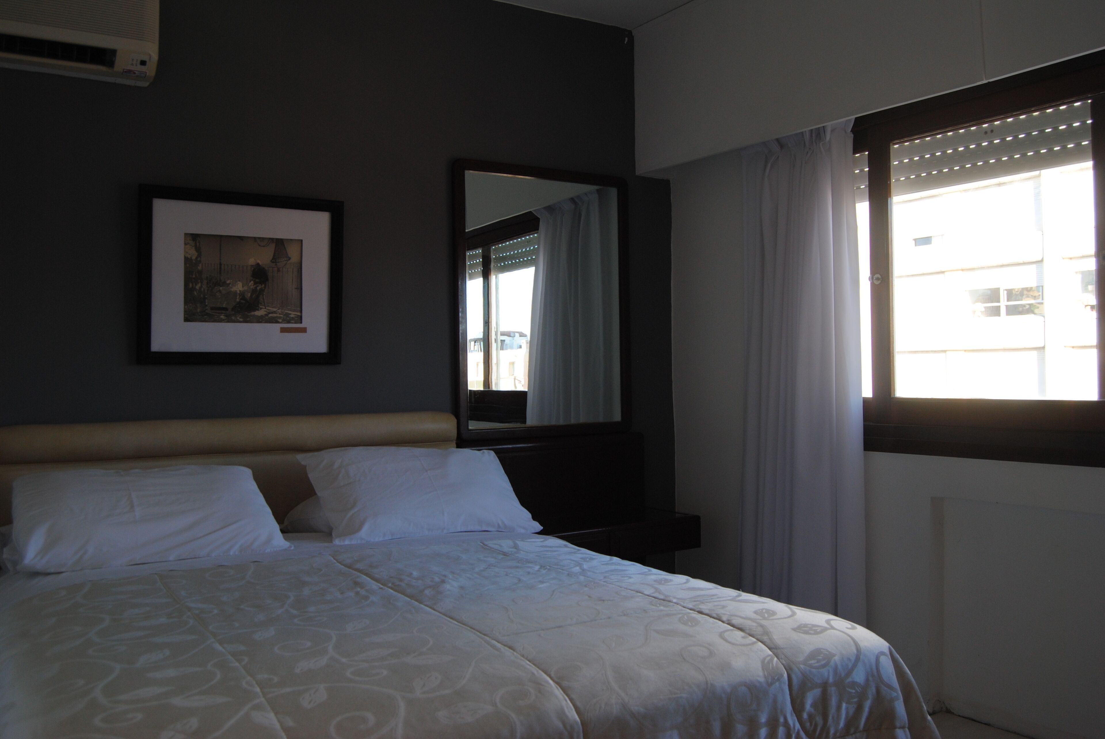 A hotel room with a bed, a framed picture on the wall, a window with curtains, and a radiator.