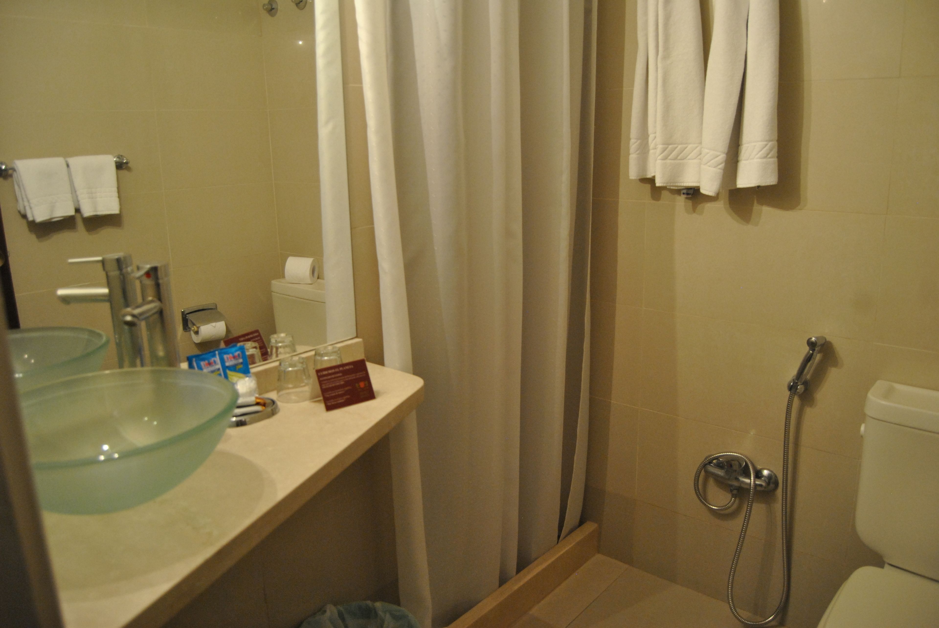 Un baño con un lavamanos de vidrio, un inodoro, una ducha con cabezal de ducha de mano y un perchero con toallas.