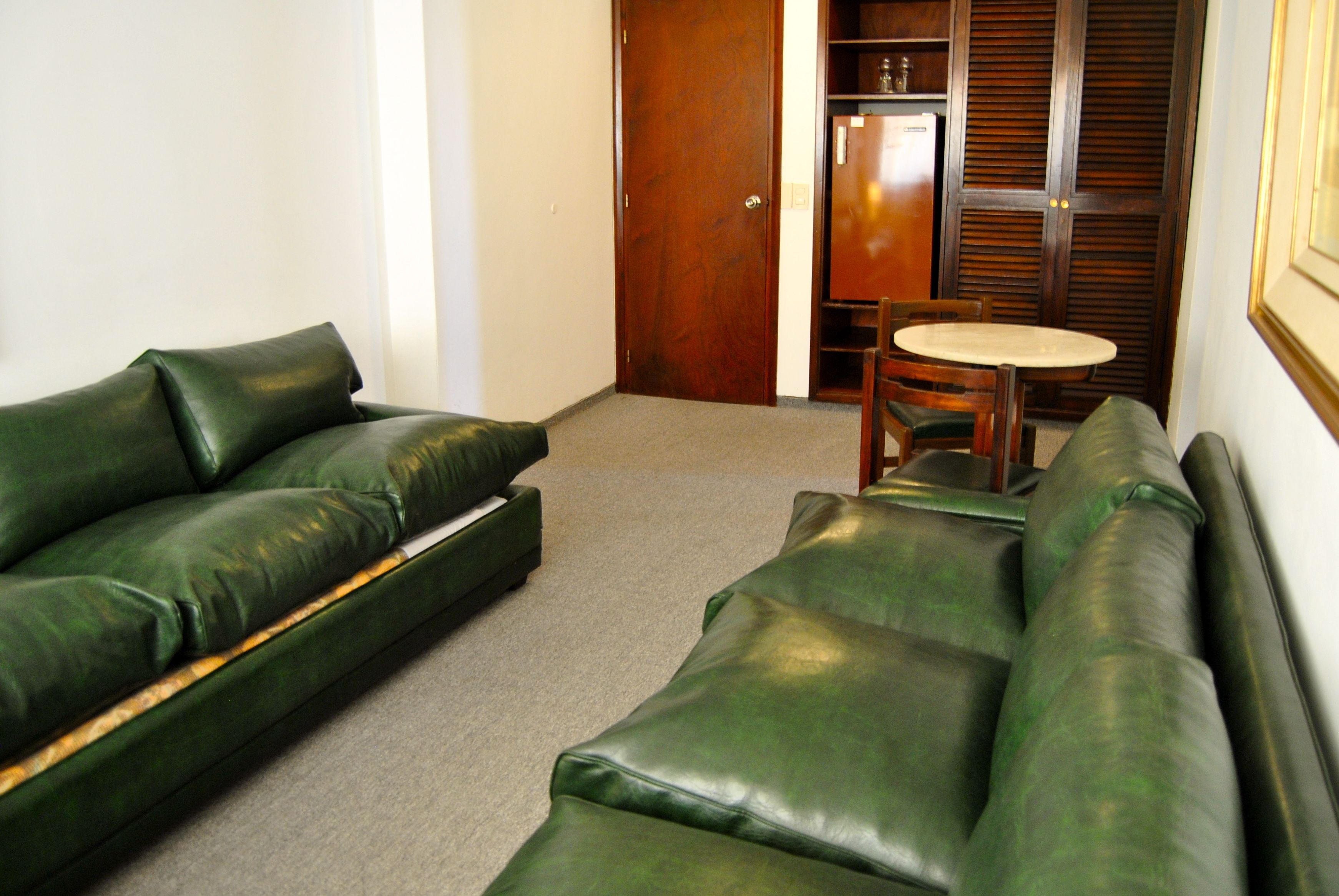 A room with a green leather sofa, a small round table, and a wooden cabinet.