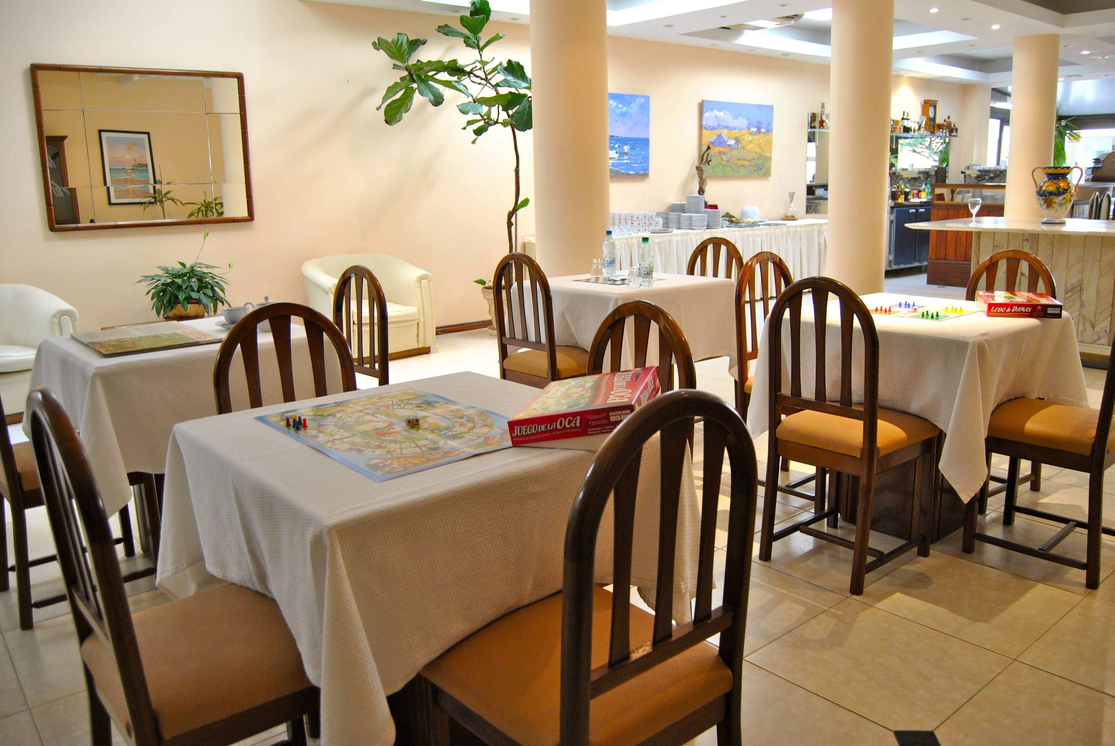 A dining area with multiple tables and chairs, a plant, and a board game.