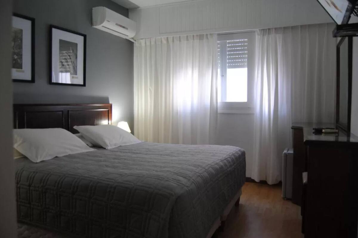 A bedroom with a bed, a desk, and a window with curtains.