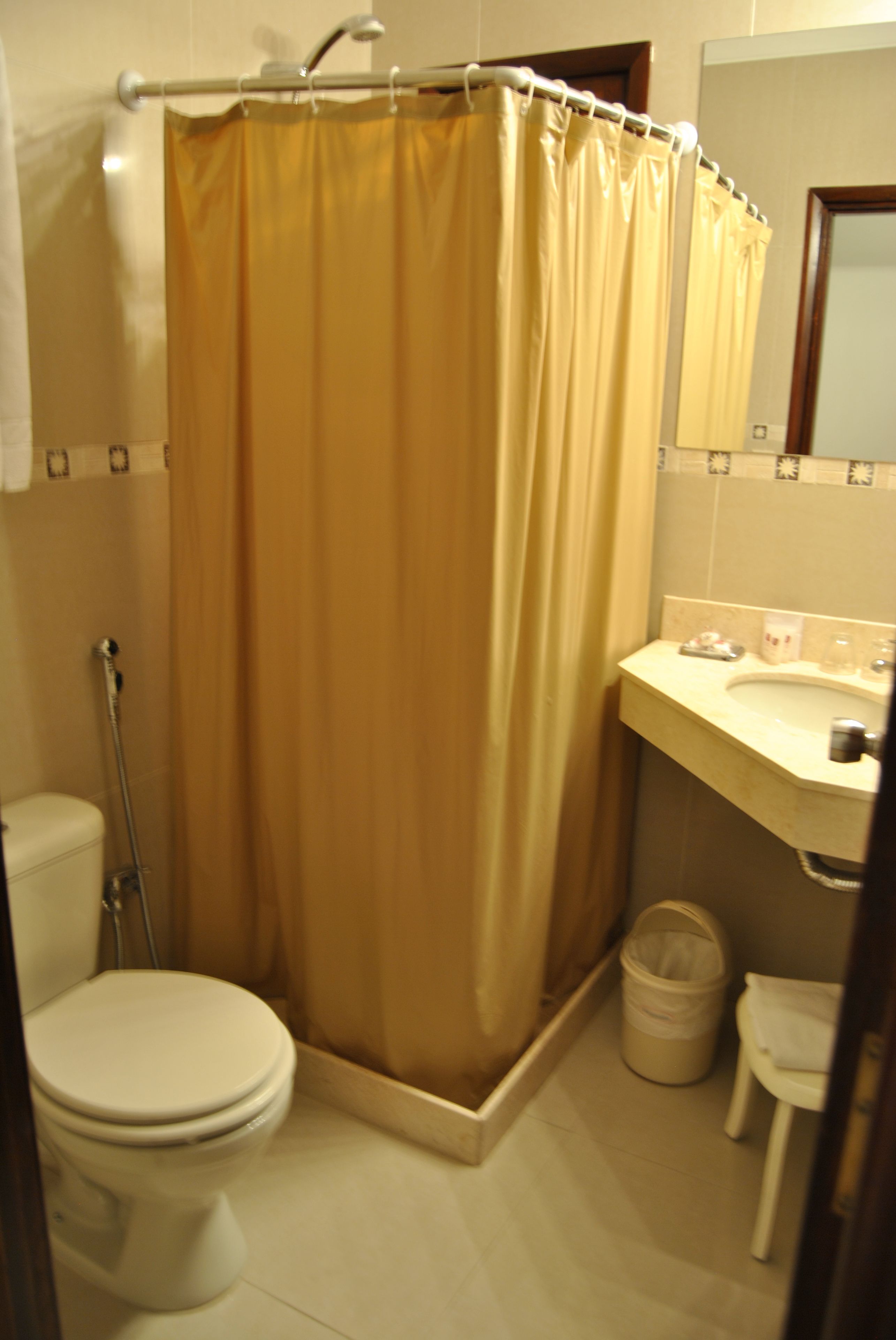 A bathroom with a shower curtain, toilet, sink, and a trash bin.