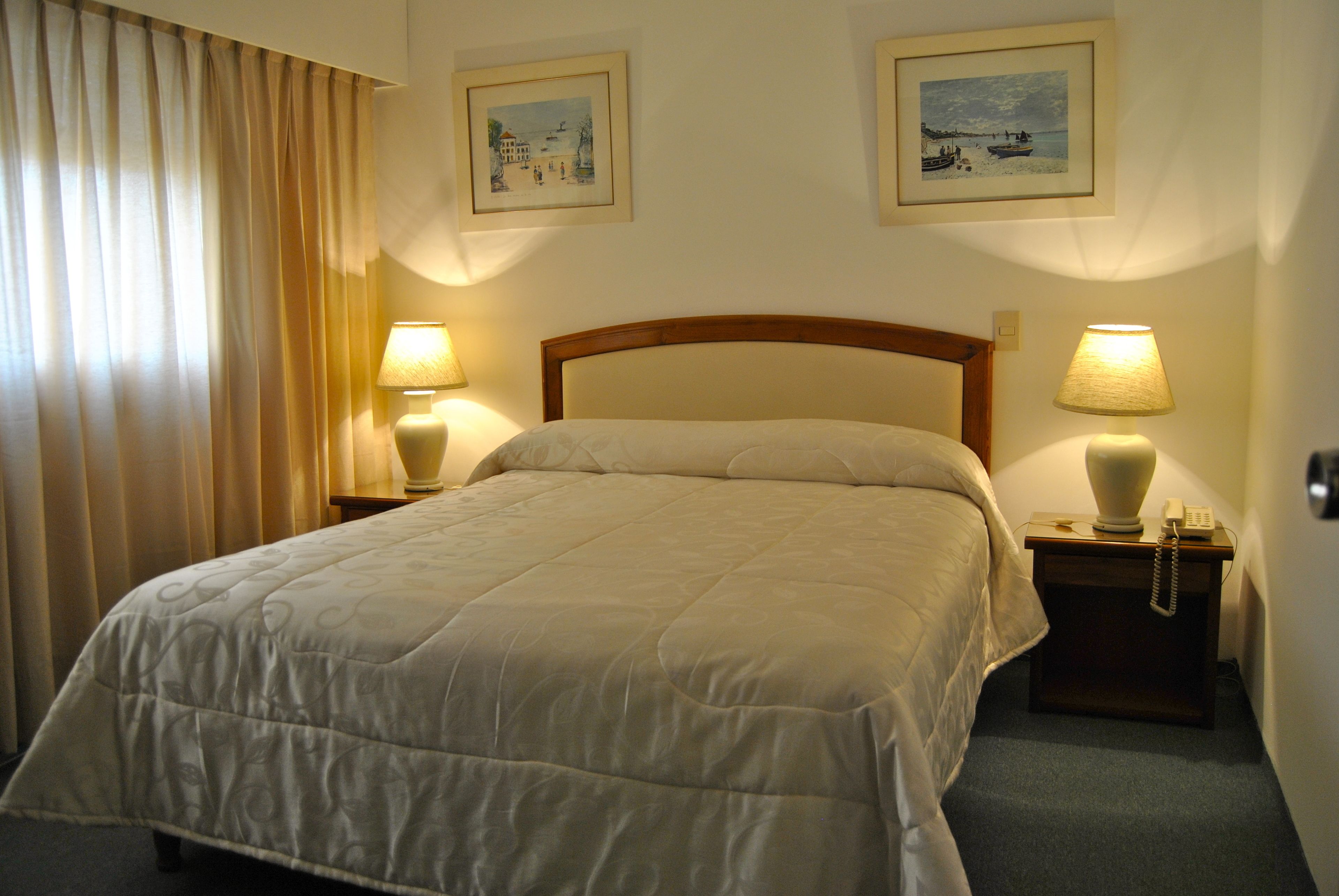 A neatly made bed in a hotel room with two bedside tables, each with a lamp and a phone.