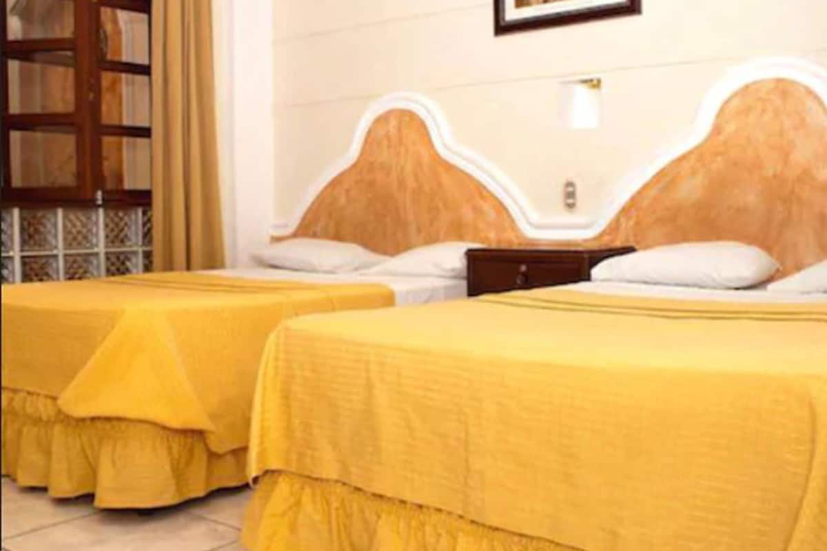 A hotel room with two beds, each with a yellow bedspread and white pillows.