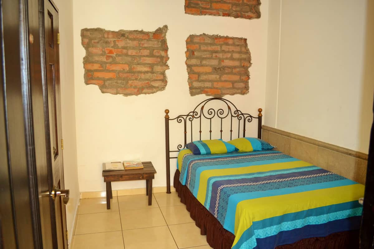 A bedroom with a bed, a nightstand, and a brick wall.