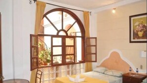 A hotel room with a bed, a small table, a chair, and a window with curtains. - Hotel Villa Florencia Centro (San Salvador)