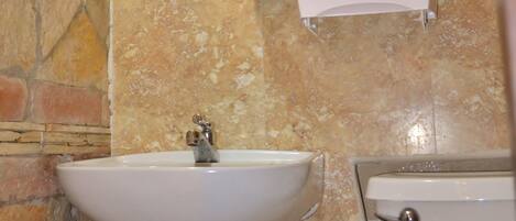 A bathroom with a sink, toilet, and a hand dryer mounted on the wall.