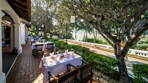 An outdoor dining area with tables set for two, overlooking a river. - Victoria Xiengthong Palace (Luang Prabang)