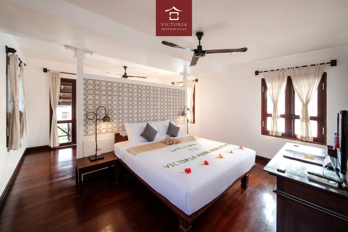A hotel room with a large bed, a desk with a computer, a ceiling fan, and a patterned wall.