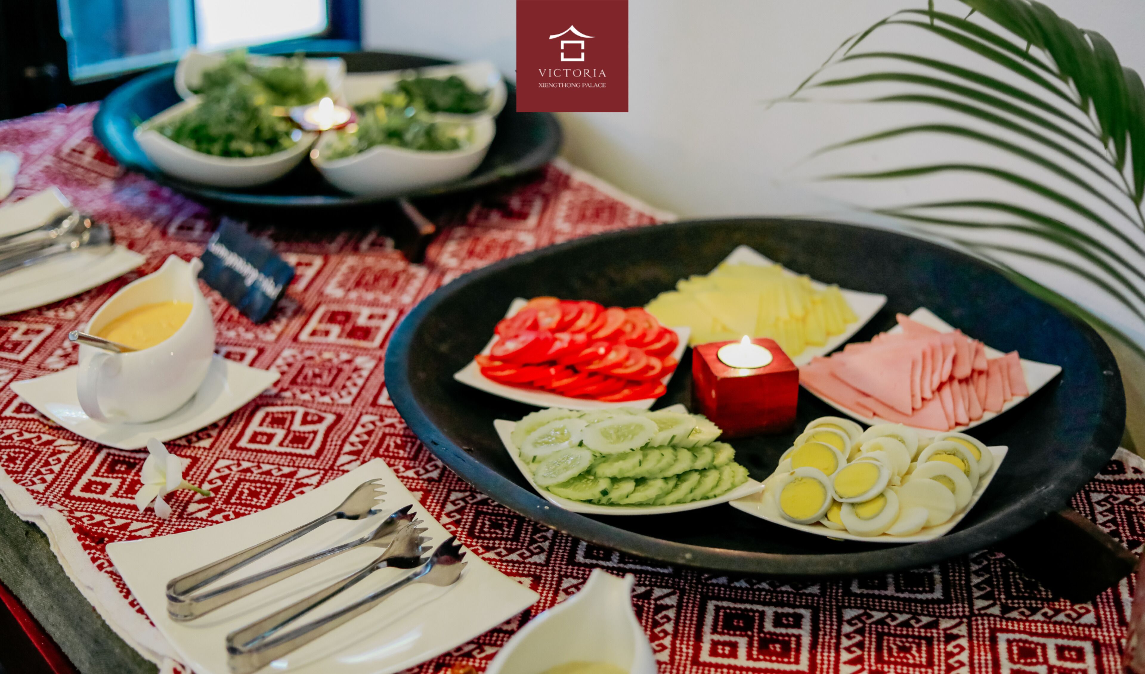 A table with various food items including sliced tomatoes, cucumbers, and eggs, with a candle and a bowl of greens in the background.