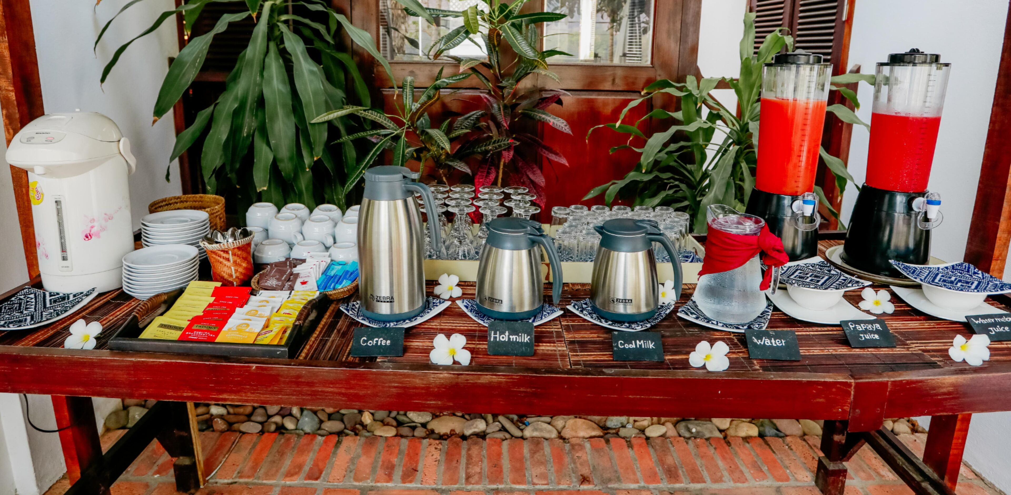 A breakfast buffet with coffee, hot milk, and cold milk options, along with various snacks and beverages.