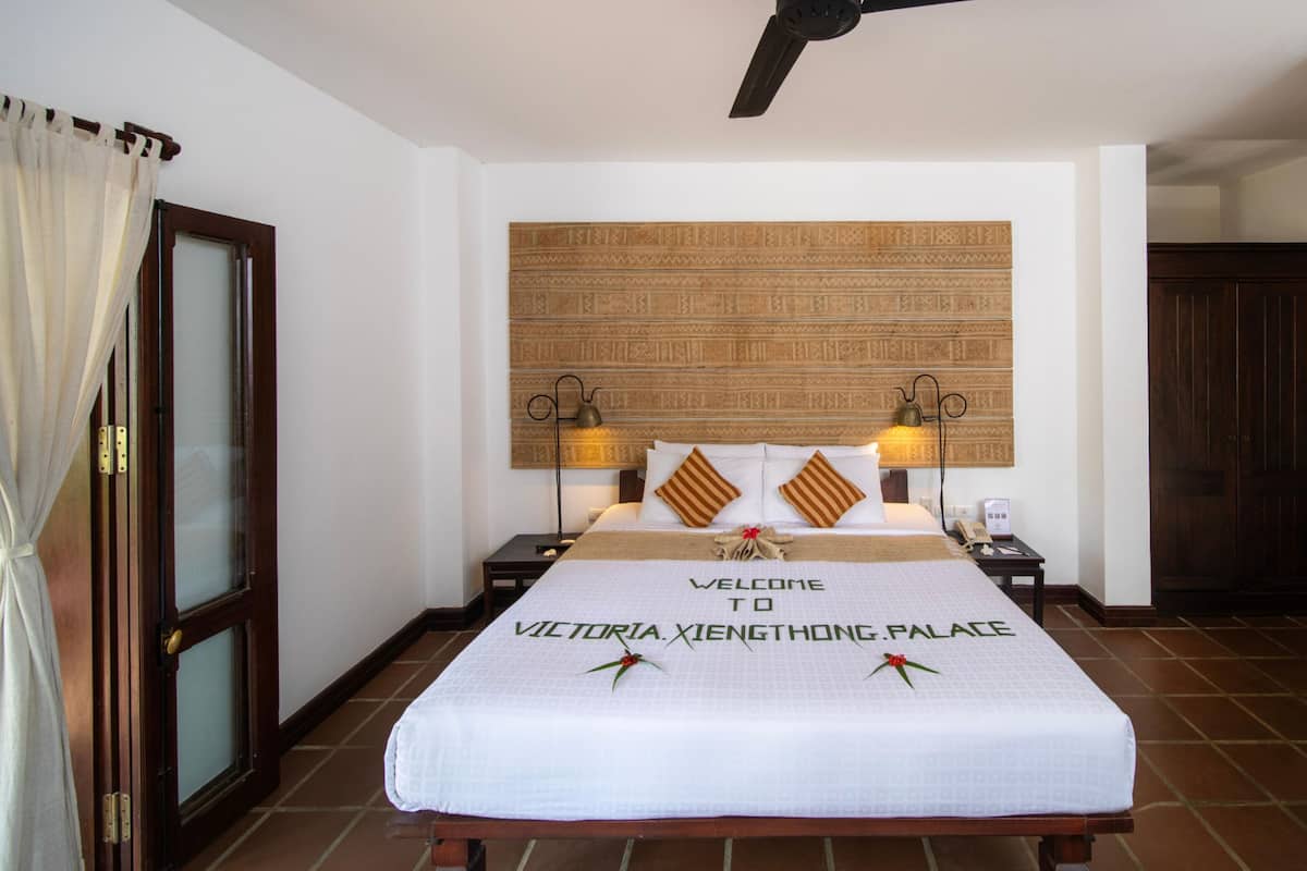 A hotel room with a bed, a wall-mounted headboard, bedside lamps, and a door with a curtain.