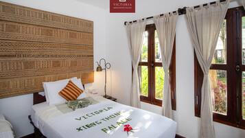 A hotel room with a bed, a headboard with a patterned design, a nightstand, a lamp, and a window with curtains.