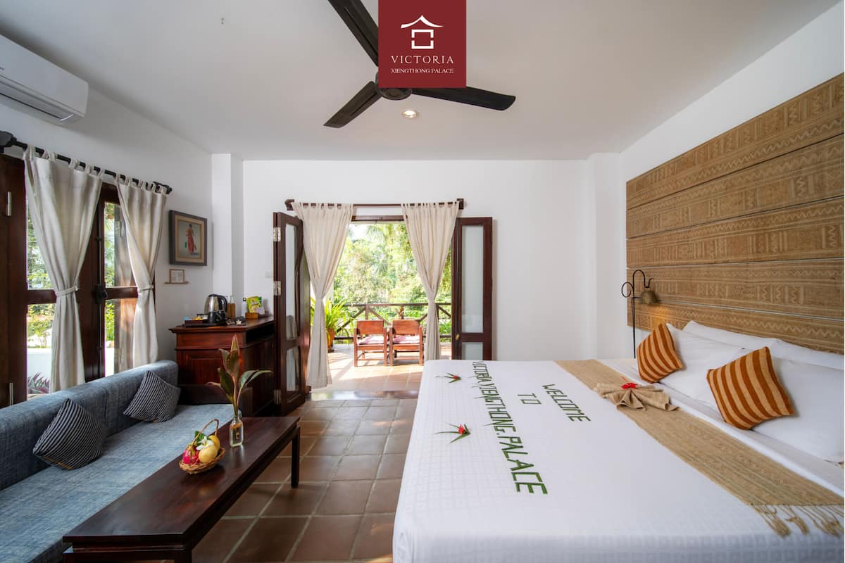 A hotel room with a bed, a sofa, a dining table, and a view of the outdoors.